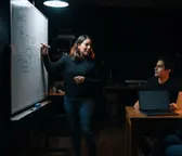 Diseñadora explicando un esquema en una pizarra durante una sesión de equipo